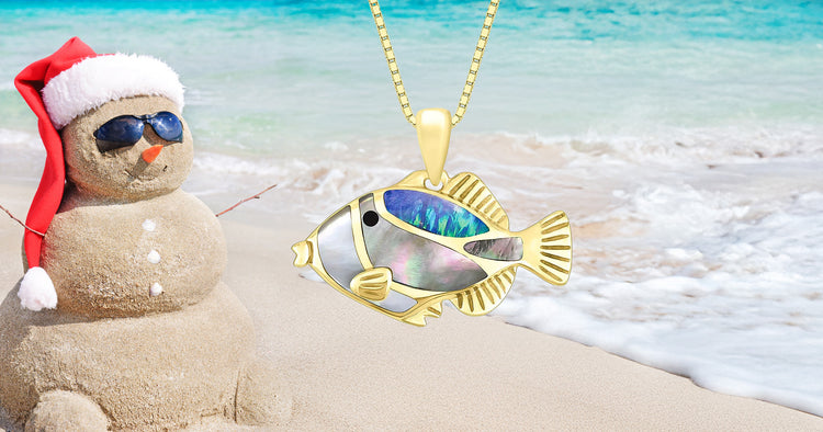 Na Keiki (Children's) Humuhumu Pendant, Item No. 44350, next to a sandy snowman on the beach